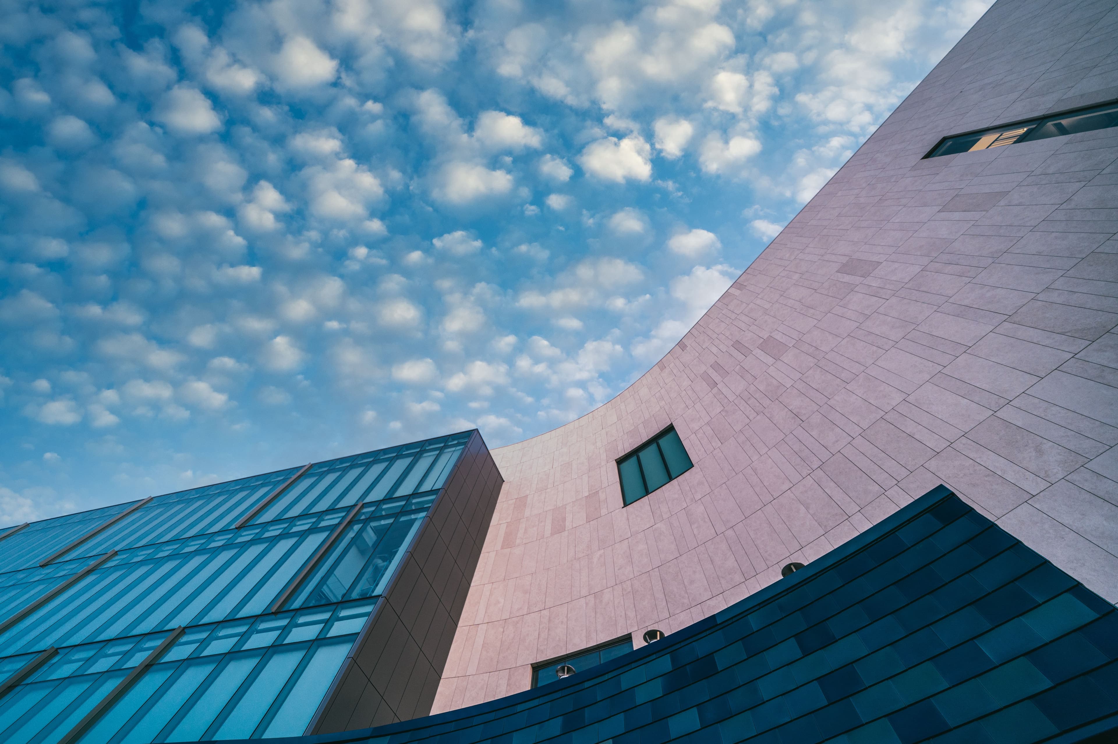 Curved stone and glass facades against a cloud-flecked sky